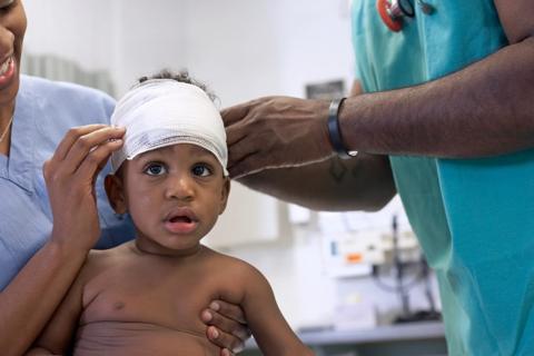 Toddler getting their head wrapped in bandage by two healthcare workers