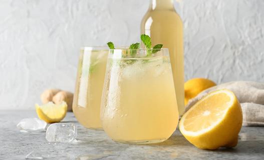 Glasses and bottle of yellow-colored prebiotic soda, with mint, lemon and ginger garnish