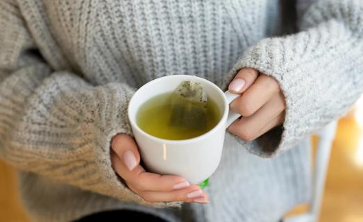 Person in bulky sweater, with their hands holding cup of tea with tea bag in it