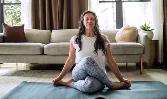 Smiling, relaxing person in a yoga pose on an exercise mat in living room