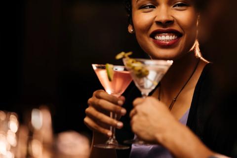 Smiling person holding martini glass, with another person's hand also holding maritini glass