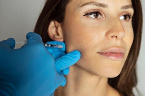 Gloved hands administering an injection into the jaw of a person