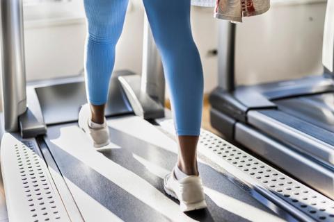 Legs and feet of person in blue leggings walking on a treadmill at gym