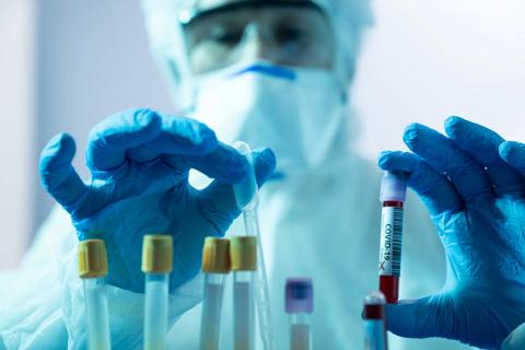 Person in mask and medical coveralls handling COVID-19 vials with gloved hands