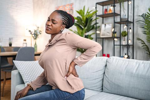 Person sitting on couch at home, with hand on lower back, grimacing