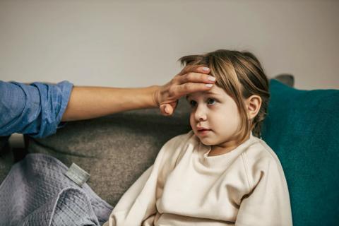 Hand feeling the temperature on the forehead of a toddler sitting on a couch