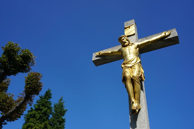 A gold Christ on a Christian Cross against a blue sky background 