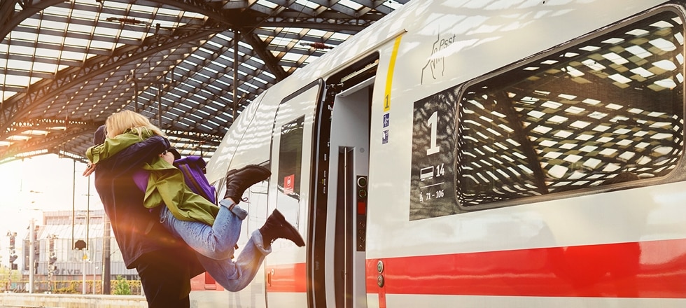 Junges Paar umarmt sich stürmisch am Bahnhof vor einem ICE 