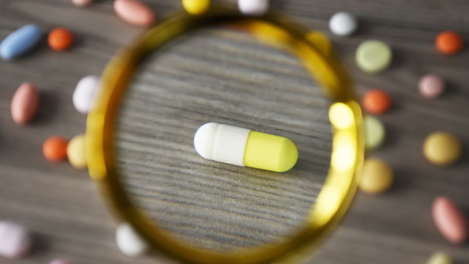 Various pills on a table with a magnifying glass over one, bringing into focus.