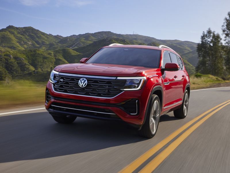 Atlas shown in Aurora Red Metallic seen from the front as it drives on a wooded mountain road.