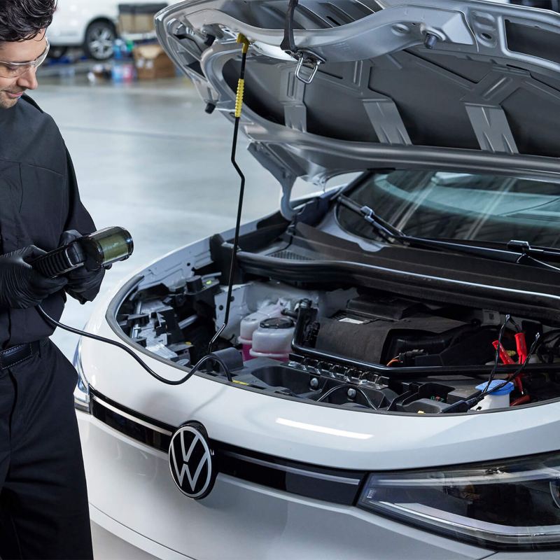 A technician stands next to an ID.4 with a diagnostic tool attached in a mechanic shop.