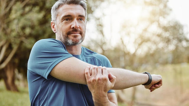 Mature man, arm stretching and outdoor for fitness, wellness and exercise in a park for health. Morning, athlete and training in nature with workout and sports of a calm person ready to start run 