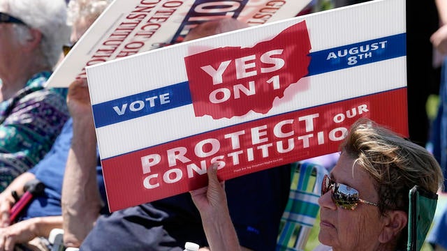 An attendee uses a sign to shield the sun during a rally on Sunday, Aug. 6, 2023, in Norwood, Ohio. 