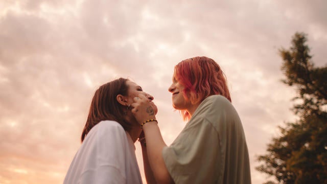 Happy young woman touching her girlfriends cheeks at sunset 