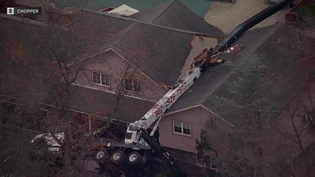 An aerial view of a truck with a crane attached to it on its side with the crane laying across the roof of a home. 