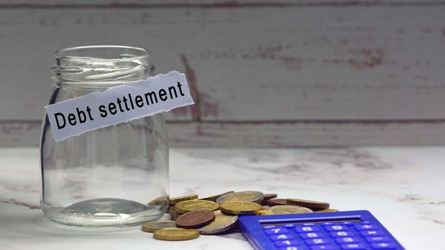 Glass jars with blurred multicurrency coins, calculator and text on white torn paper - Debt settlement 