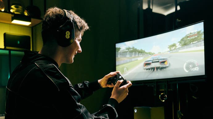 A man plays Grid Legends in front of a curved monitor, holding an Xbox controller.