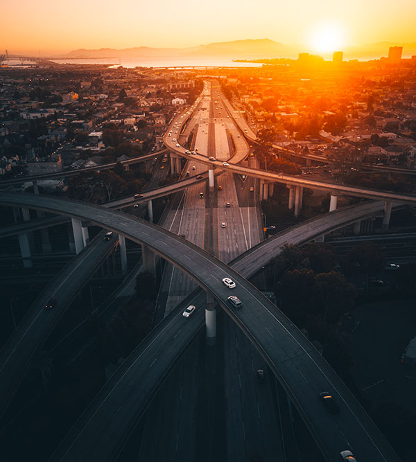 日落时分高速公路立交桥的鸟瞰图，道路上汽车行驶，背景是城市天际线。.