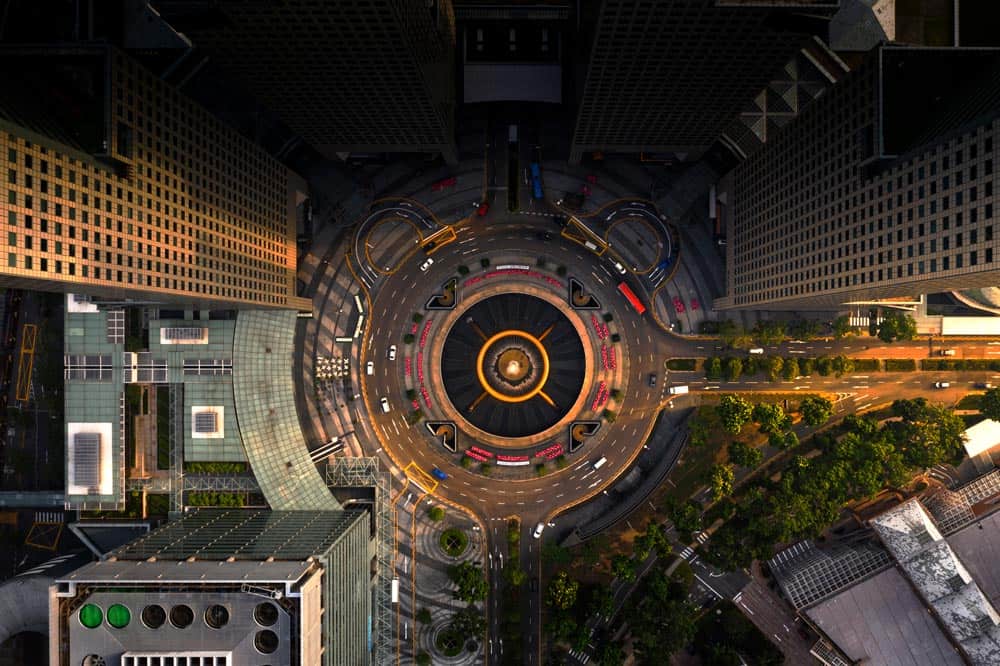 Aerial view of a circular roundabout designed by skilled civil engineers, surrounded by tall buildings, with roads and green areas seamlessly integrated.