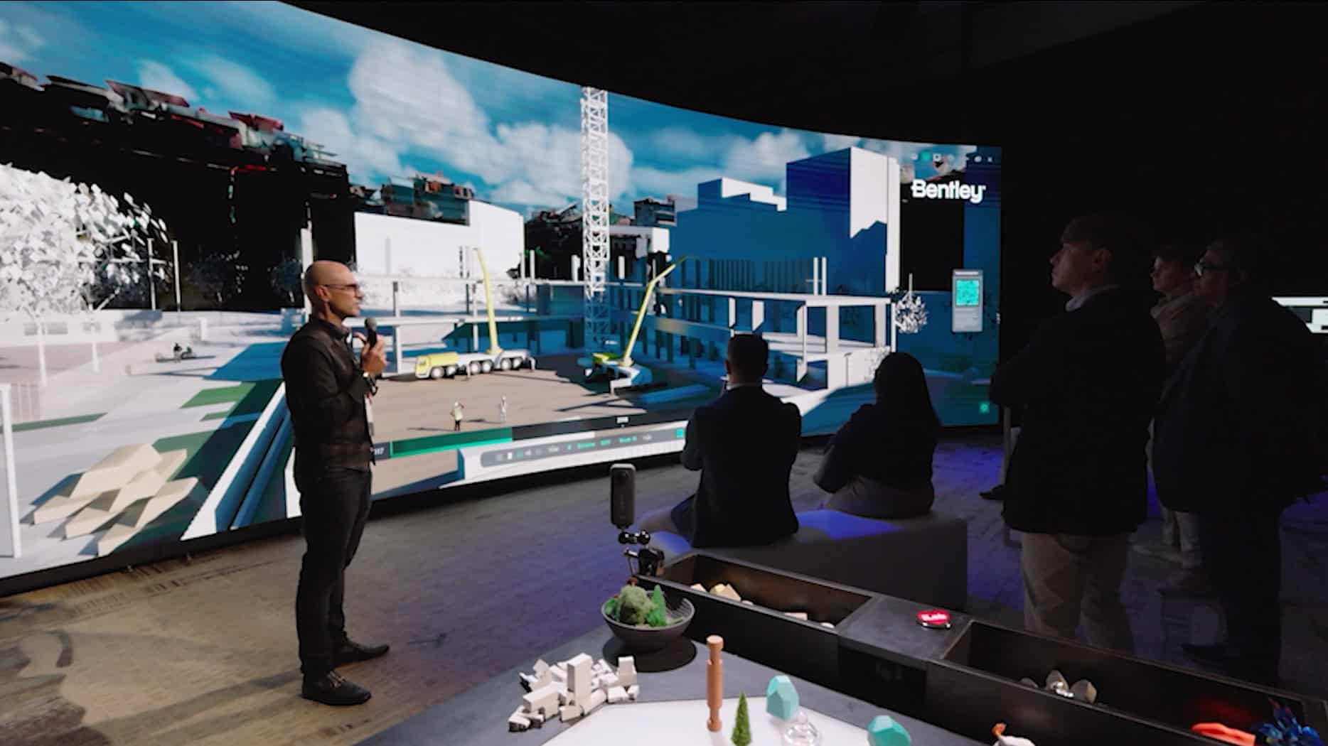 Greg Demchak, Bentley’s vice president for emerging technologies presents in a room with a large curved screen displaying a digital construction site to an audience.