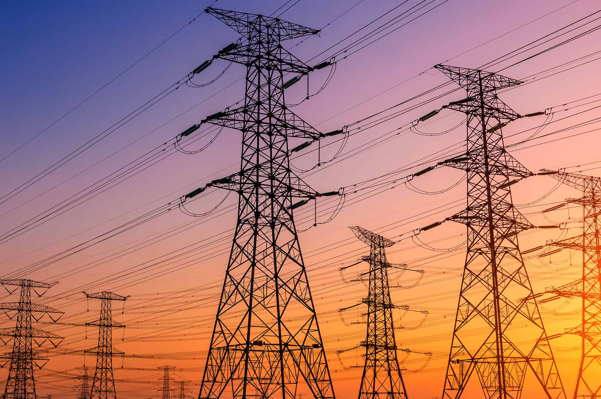 Silhouettes of transmission towers against a vibrant sunset sky.