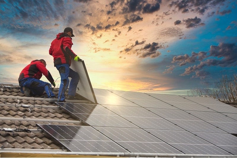 Two technical specialists are installing solar panels on the roof.