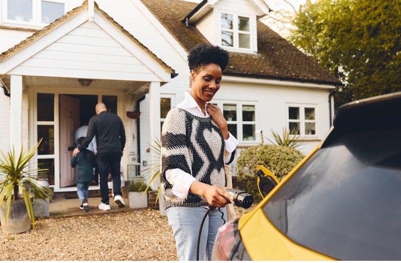 A woman is charging her EV while her husband and kid are walking to home.