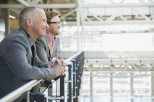 Two smiling businessmen leaning on a railing, looking out over an atrium.