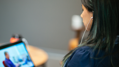 Erika Martinez, a woman who is hard of hearing, wears headphones and watches a video on a laptop.