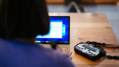 Anne Taylor seated at a table uses a laptop with a braille keyboard.