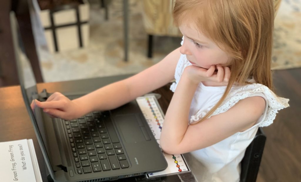 Kindergarten age girl touching a computer screen.