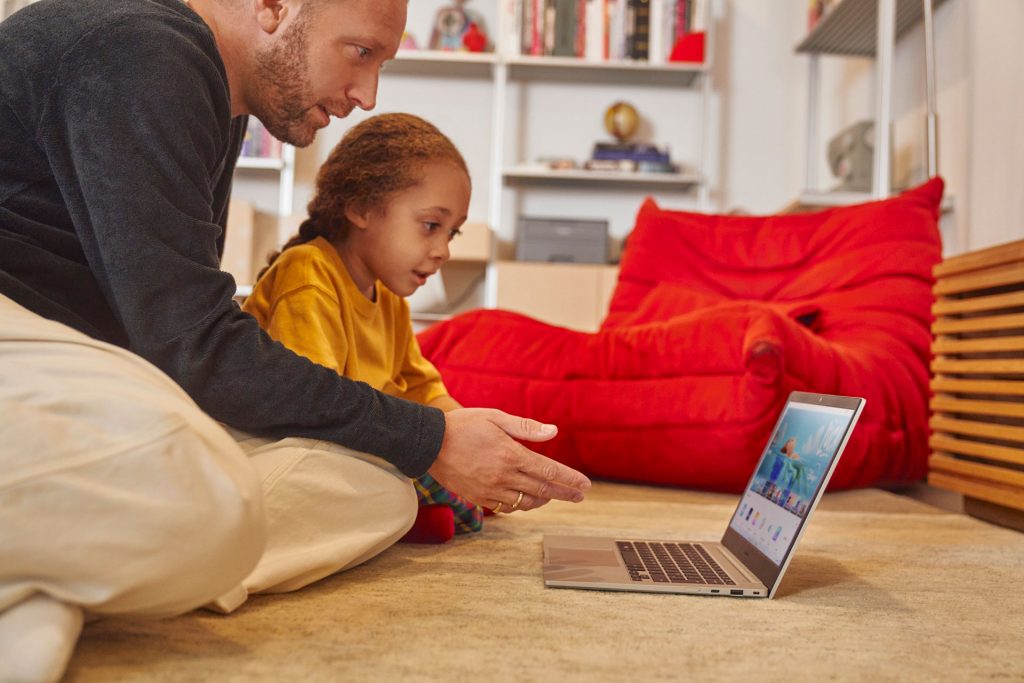 Father and daughter sitting on the floor enjoying what's on their laptop computer