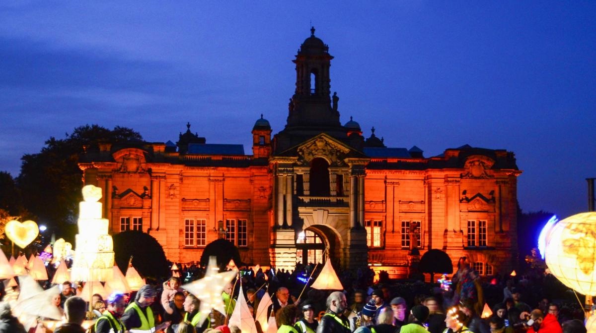 Exterior of Cartwright Hall Art Gallery at night, illuminated and with a crowd holding lanterns in front