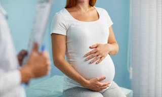 Pregnant woman with hands on stomach talking to obstetrician-2015