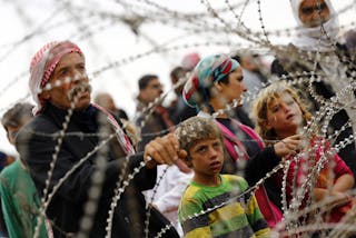 Syrian Kurds wait behind the border fences to cross into Turkey near the southeastern town of Suruc in Sanliurfa province