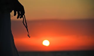 Silhouette of a man with a rosary in his hands at sunset — Photo by jahmaica