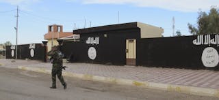 An Iraqi Shi'ite fighter walks past walls painted with the Islamist State flag in Saadiya