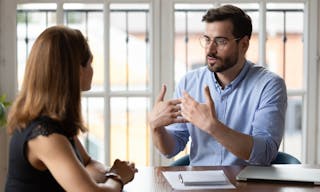 Confident male boss leader in eyeglasses explaining project details to new female employee at meeting. Concentrated young woman 