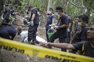 Policemen monitor as forensic experts dig out human remains near the abandoned human trafficking camp in the jungle close the Th