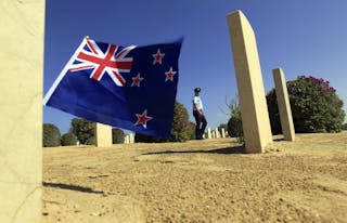 A soldier walks amongst graves of World War Two soldiers and past a New Zealand flag after a ceremony to mark the 70th anniversa