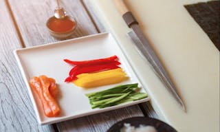 Raw fish and sliced paprika. Knife beside plate with vegetables. Fresh ingredients for sushi rolls. Pieces of ripe bell pepper.