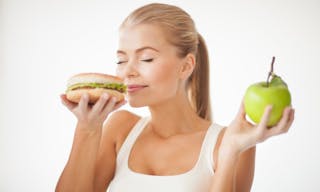 healthy woman smelling hamburger and holding apple