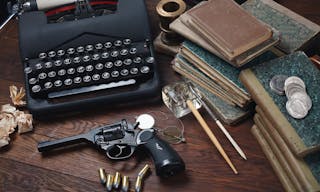 Writing a detective story - old retro vintage typewriter and revolver gun with ammunitions, books, papers, old ink pen on wooden