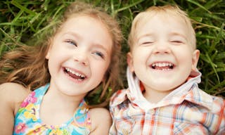 Top view portrait of two happy smiling kids lying on green grass. Cheerful brother and sister laughing together. - 圖片