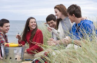 Teenage friends enjoying barbecue in grass on beach