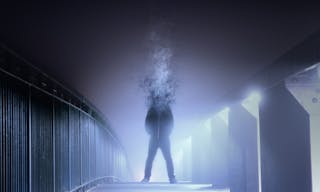 A conceptual digital art picture of a man whos head has disintergrated and turned into smoke, standing on a foggy path at night.