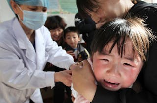 A girl cries in her mother's arm while receiving a vaccination from a nurse at a hospital in Huaibei