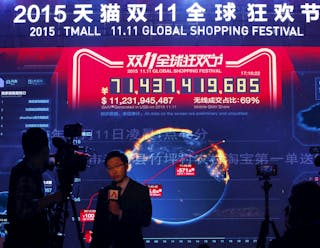 A TV reporter is filmed in front of  a screen showing real-time data of transactions during Alibaba Group's 11.11 Global shoppin