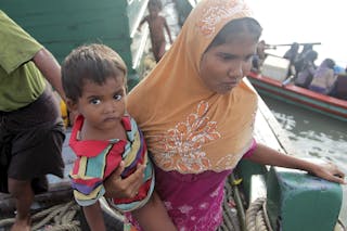 Rohingya migrant carrying a child stands onboard a fishing boat before being transported to shore, off the coast of Julok, in Ac