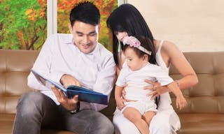 Portrait of two parents sitting on sofa and read book with their daughter, autumn on the window